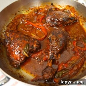 Authentic Jamaican Brown Stew Chicken Recipe 9 Brown stew chicken in a pot with gravy and peppers.