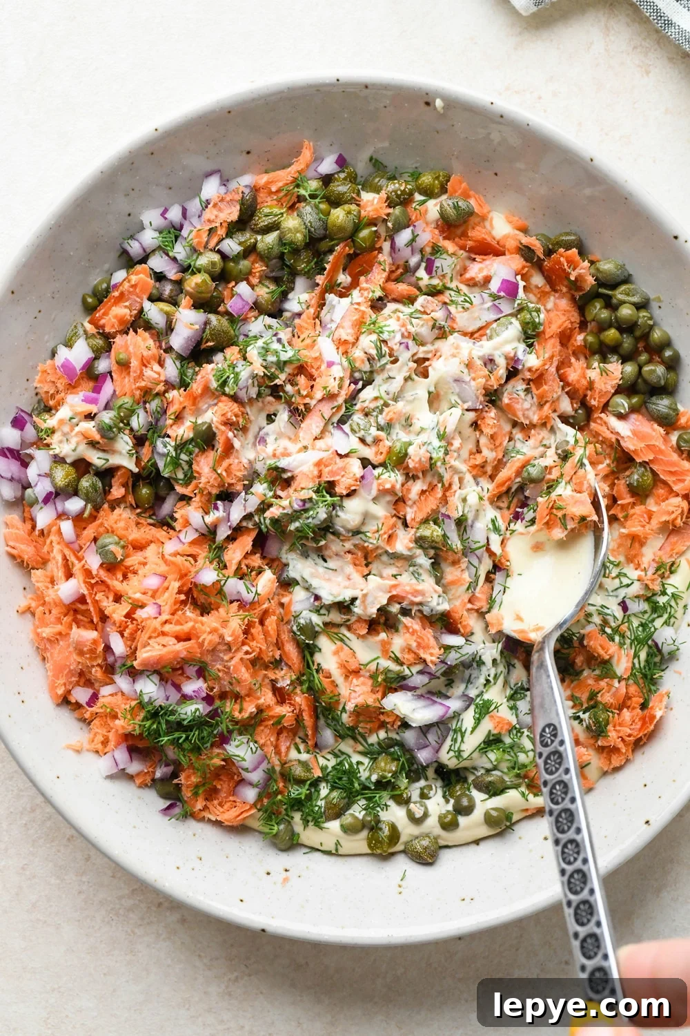 How to make dairy free smoked salmon dip: Mixing the smoked salmon, capers, dill, and red onion into the cashew cream base.