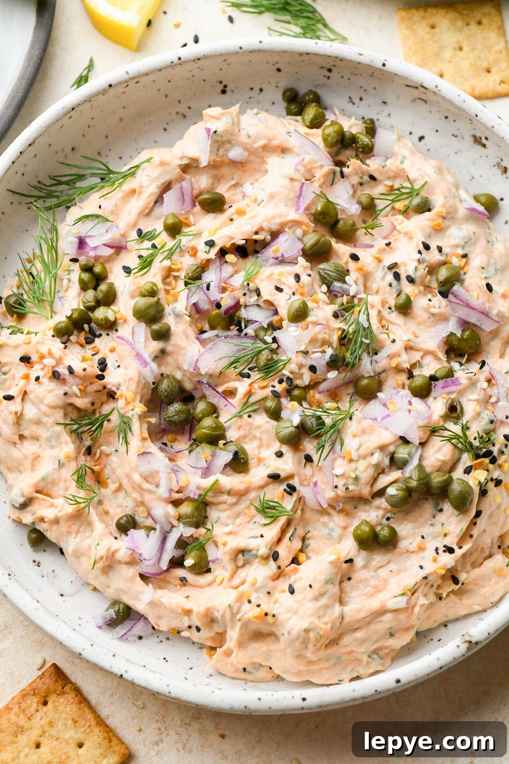 Dairy free smoked salmon dip in a small shallow ceramic speckled bowl, garnished with capers, fresh dill, everything but the bagel seasoning.