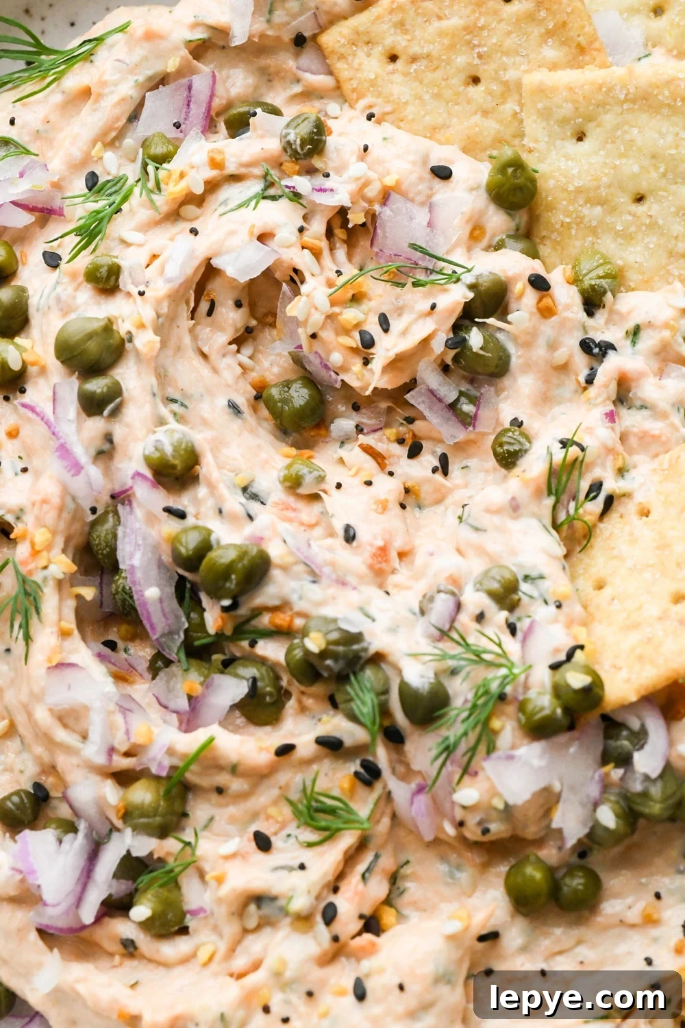 Close up shot of the texture of dairy free smoked salmon dip after a cracker has scooped some of the dip out of the bowl.