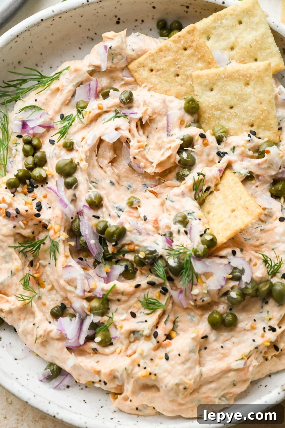 Dairy free smoked salmon dip in a shallow bowl topped with garnishes, after a cracker has scooped some of the dip out of the bowl.