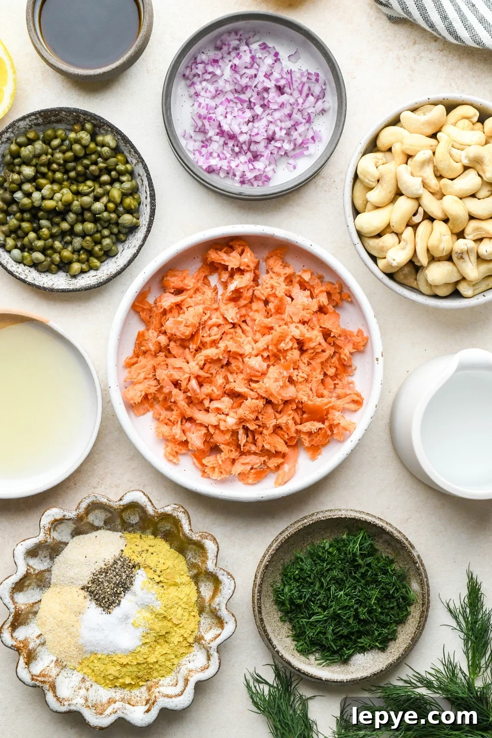 Ingredients for dairy free smoked salmon dip in various ceramics on a light cream colored background.