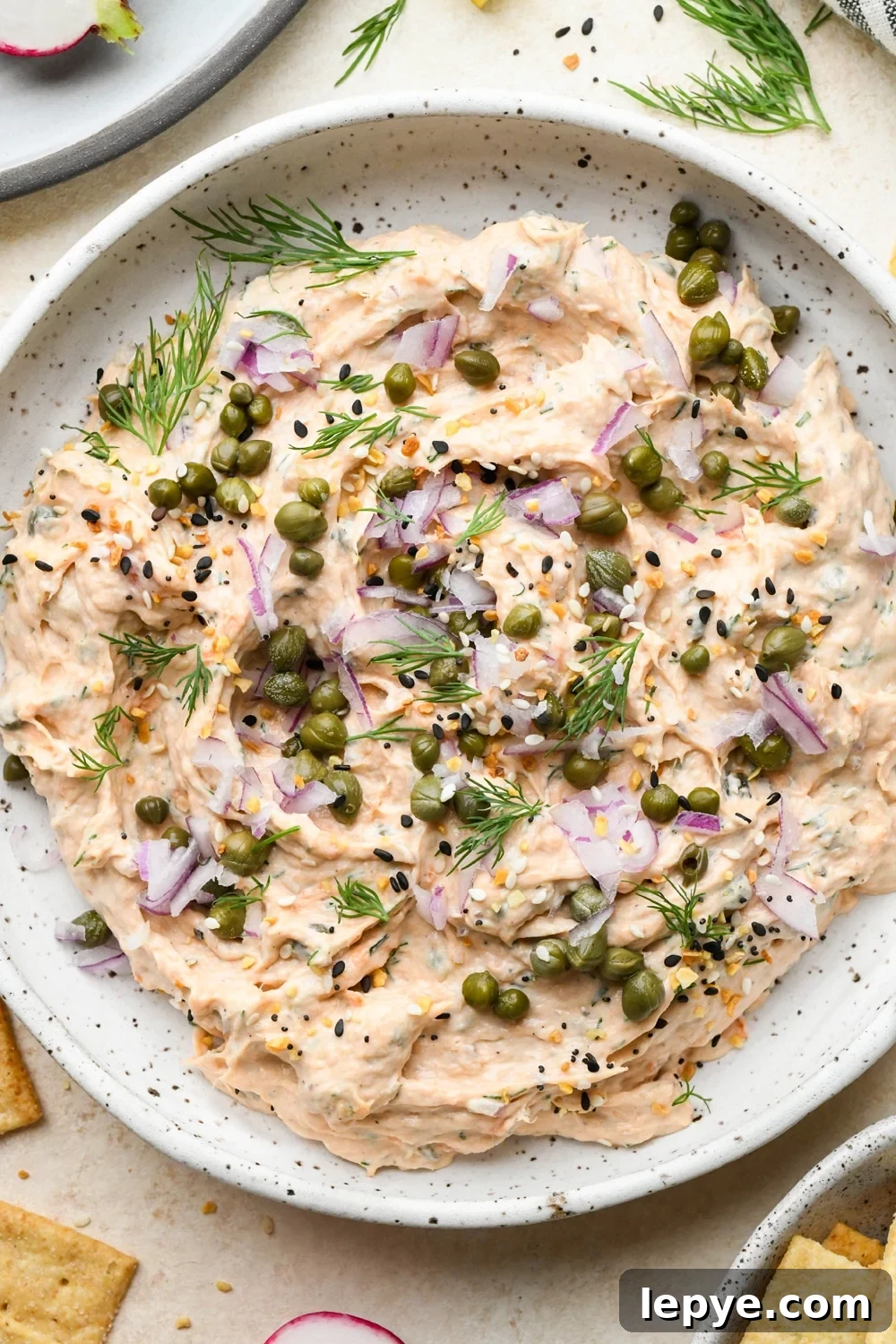 Dairy free smoked salmon dip in a small shallow ceramic speckled bowl, garnished with capers, fresh dill, everything but the bagel seasoning.