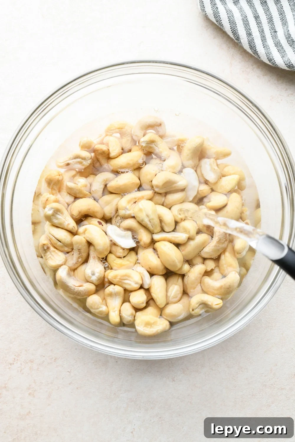 How to make dairy free smoked salmon dip: A hot water kettle pouring boiling water over raw cashews in a medium-sized glass bowl.