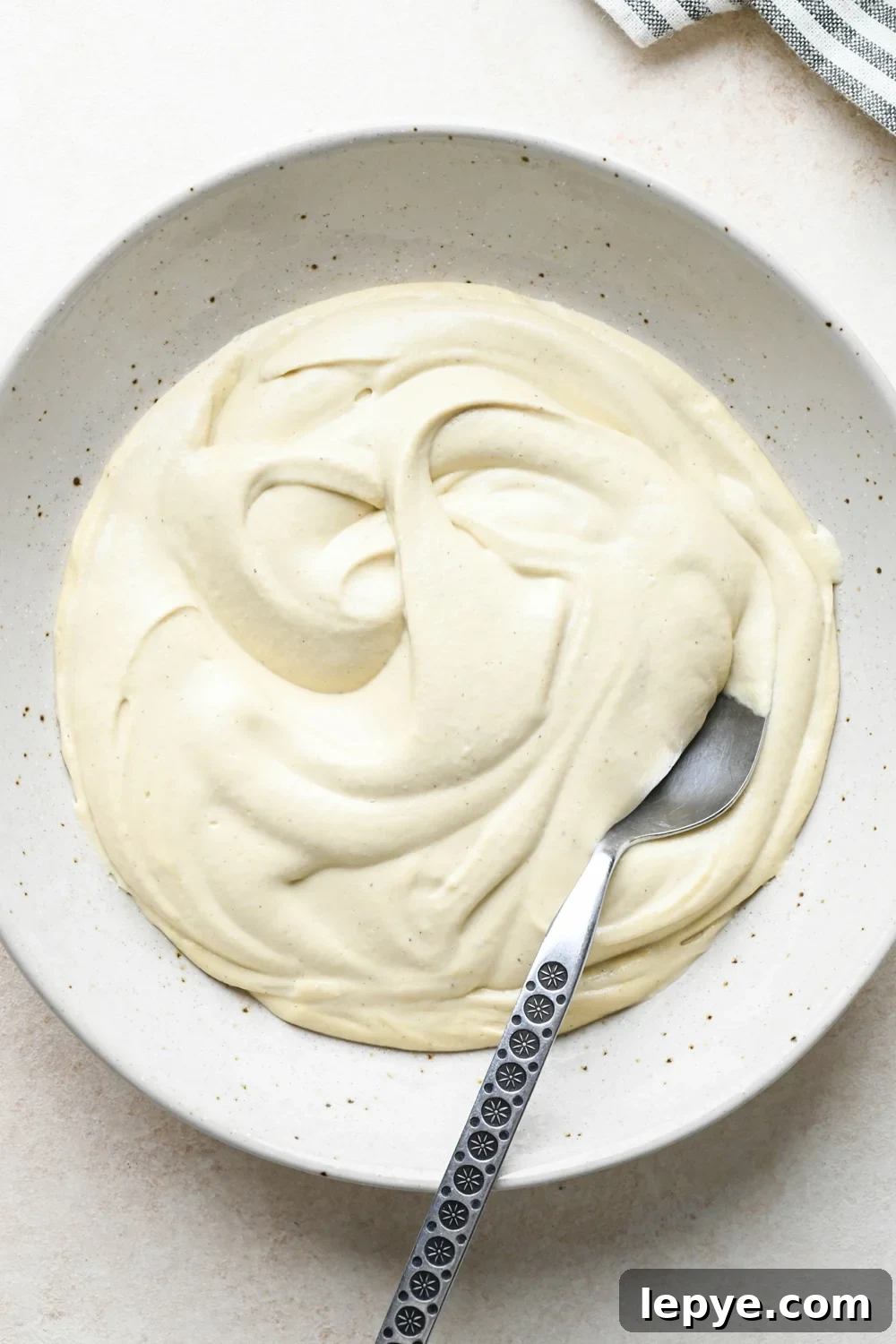 How to make dairy free smoked salmon dip: Cashew cream base in a large shallow bowl with a spoon.