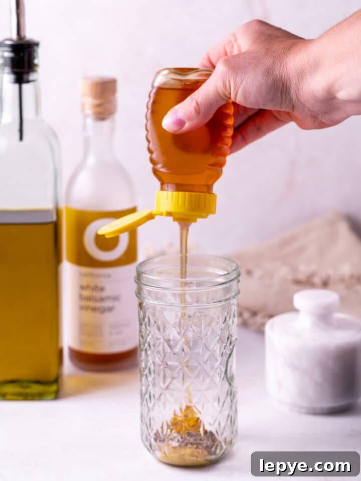 White Balsamic Vinaigrette Recipe: Tangy Salad Dressing with Herbs 4 hand squeezing honey into a mason jar