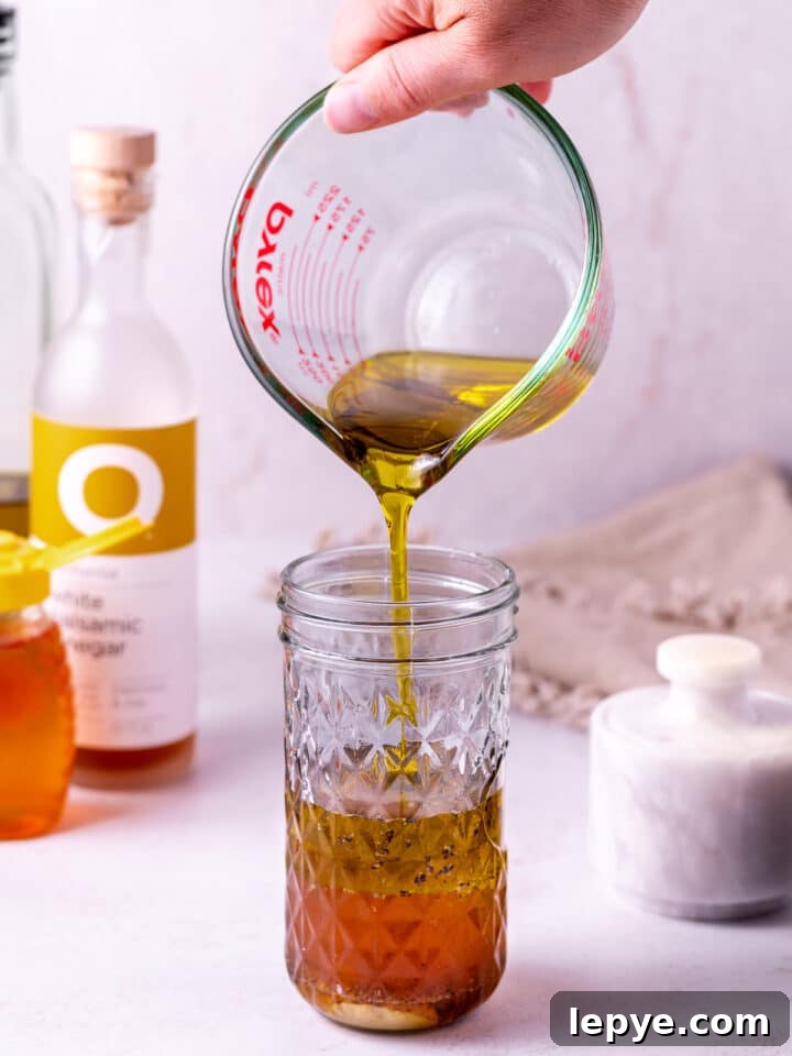 White Balsamic Vinaigrette Recipe: Tangy Salad Dressing with Herbs 6 hand pouring olive oil from a liquid measuring cup into a mason jar with other salad dressing ingredients