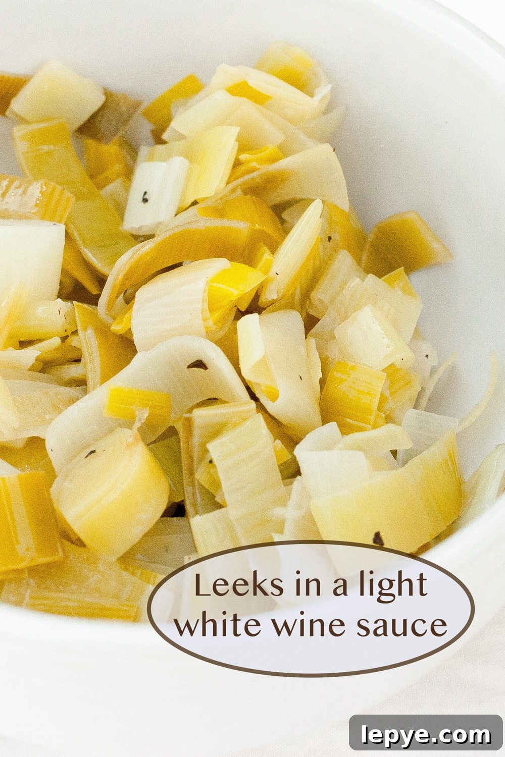 Braised Leeks in Creamy White Wine Sauce 2 cooked leeks in a white bowl.