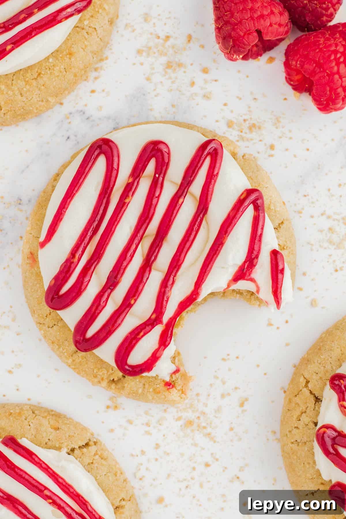 Raspberry Cheesecake Cookie Recipe — Soft, Jam-Filled Treats 2 A raspberry cheesecake cookie on a white countertop with a bite taken out of it.