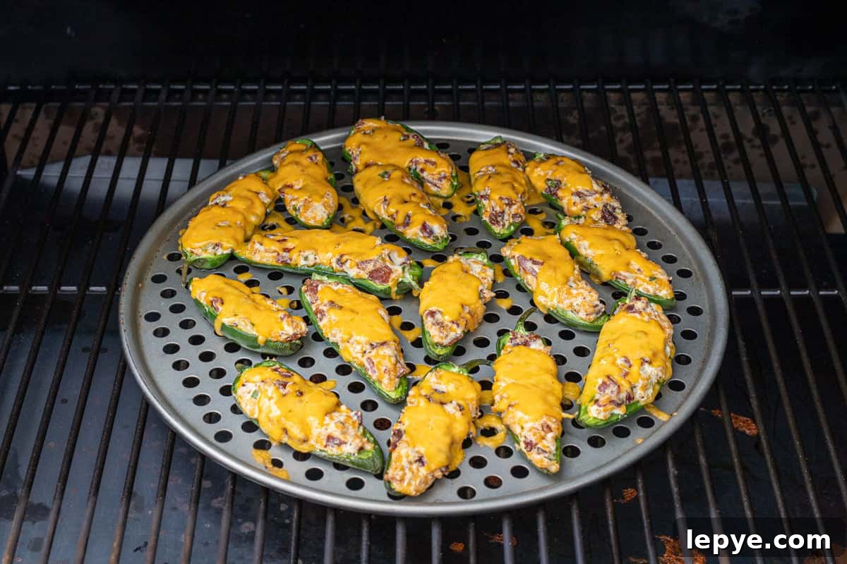 Smoked Jalapeño Poppers Recipe for Perfect Grill Parties 10 Freshly smoked jalapeno poppers on a pizza pan on a grill grate on a smoker.