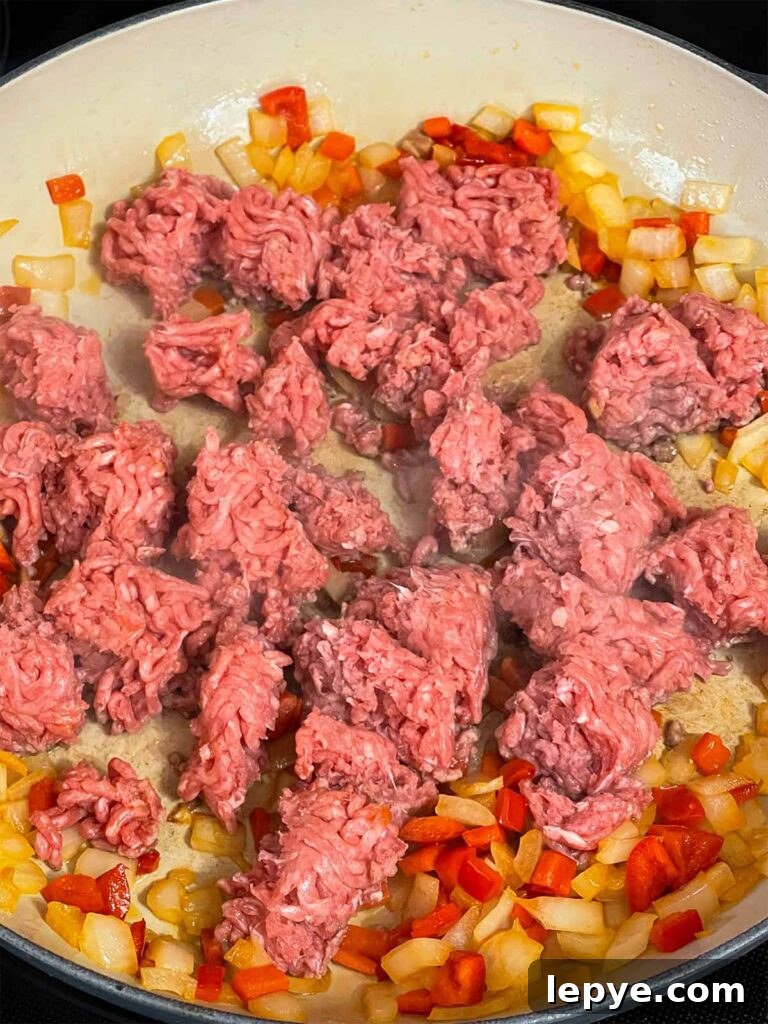 Ground beef added to onions and red bell pepper in a skillet.