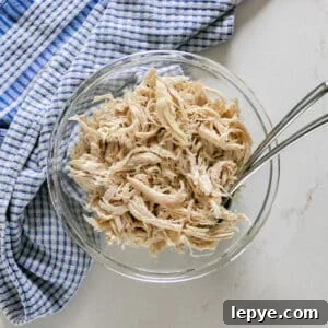 Shredded Chicken Recipes: Crockpot and Instant Pot Guide 12 An overhead image of shredded chicken breast in a glass bowl with a blue checked towel next to it and a couple of forks in it.