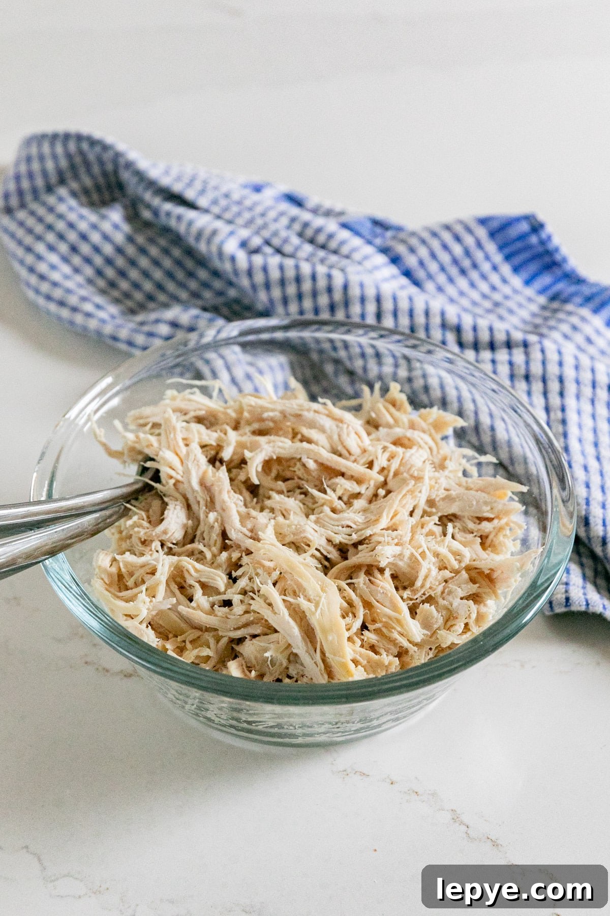 Shredded Chicken Recipes: Crockpot and Instant Pot Guide 7 A bowl of shredded chicken with two forks sticking out and a blue checked towel behind it.