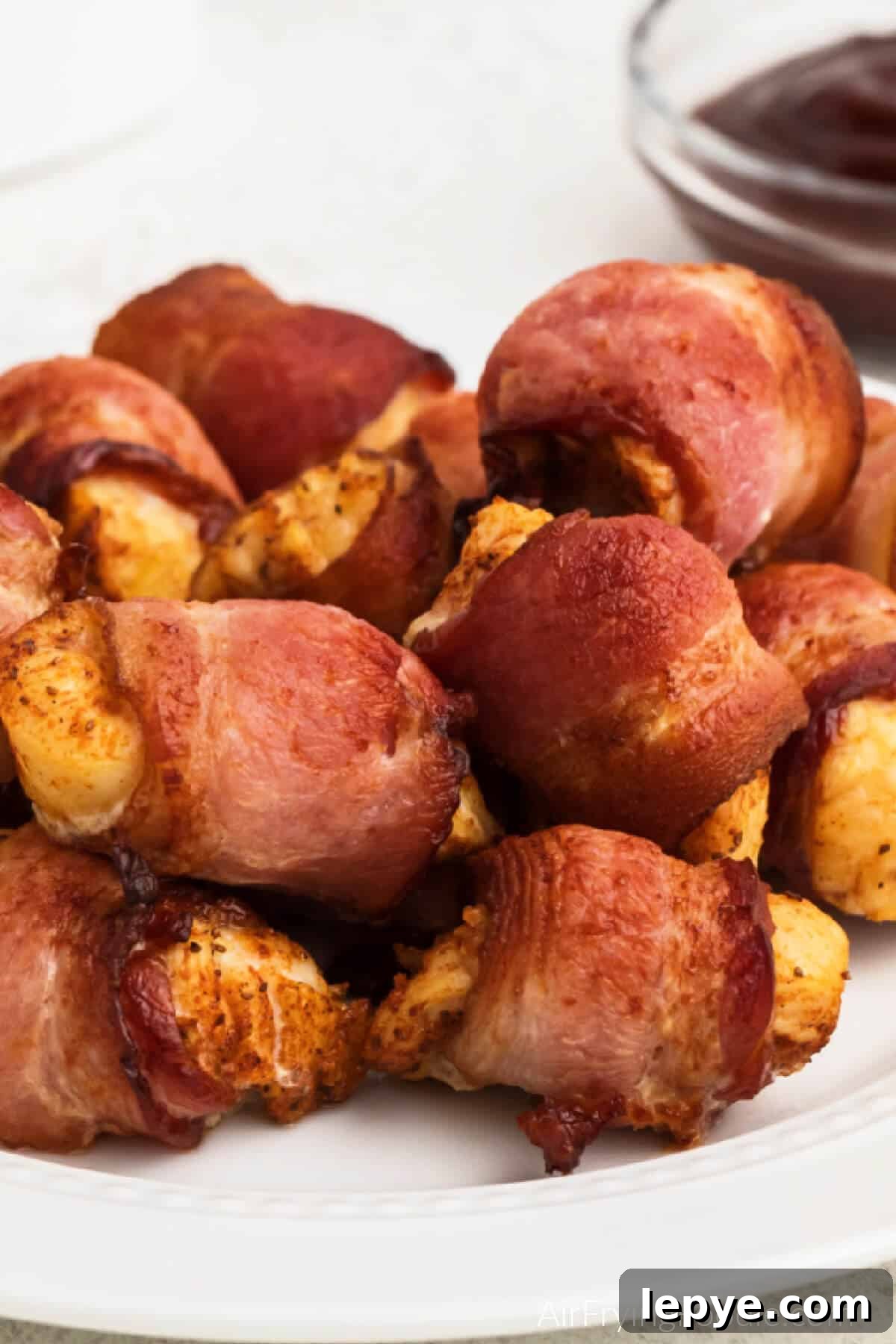 Crispy Bacon-Wrapped Chicken Bites Made in the Air Fryer 2 Bacon wrapped chicken bites made in the air fryer and served on a white plate.