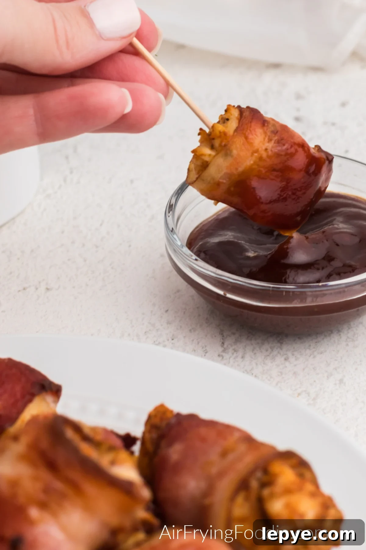 Crispy Bacon-Wrapped Chicken Bites Made in the Air Fryer 3 Bacon wrapped chicken bites being dipped in BBQ sauce.