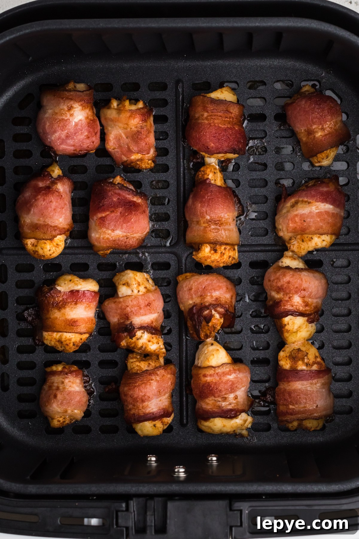 Crispy Bacon-Wrapped Chicken Bites Made in the Air Fryer 5 Fully cooked bacon wrapped chicken bites in the basket of the air fryer.