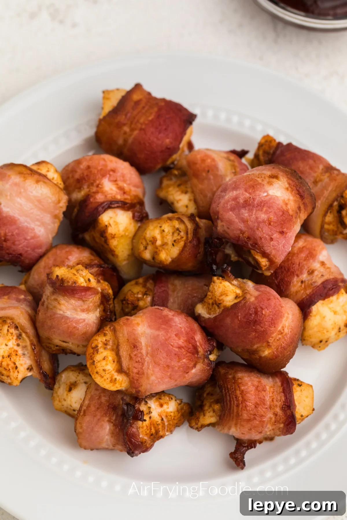Crispy Bacon-Wrapped Chicken Bites Made in the Air Fryer 6 Bacon wrapped chicken bites on a white plate ready to serve.