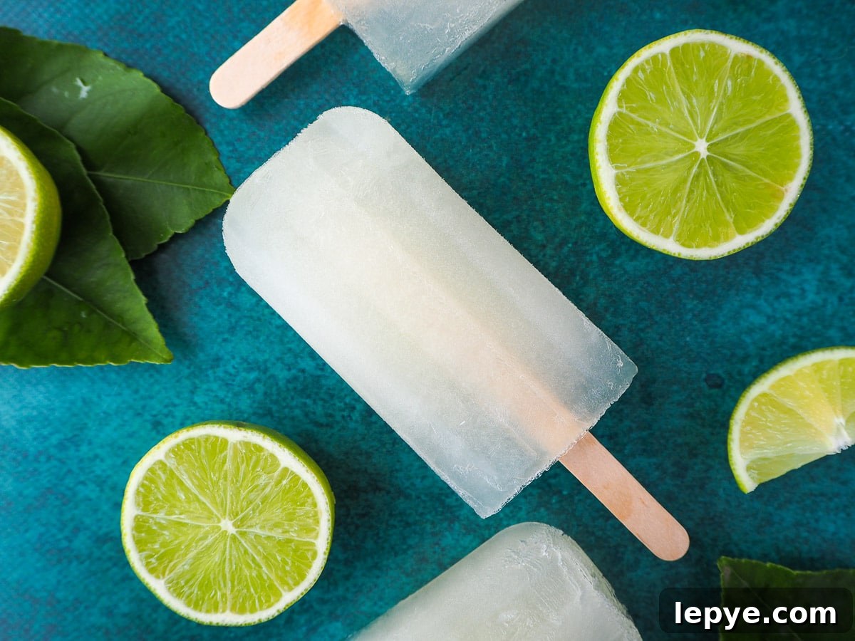 Refreshing Lime Popsicle Recipe: Homemade Citrus Ice Pops 2 Lime popsicles surrounded by fresh cut limes, on a green background.