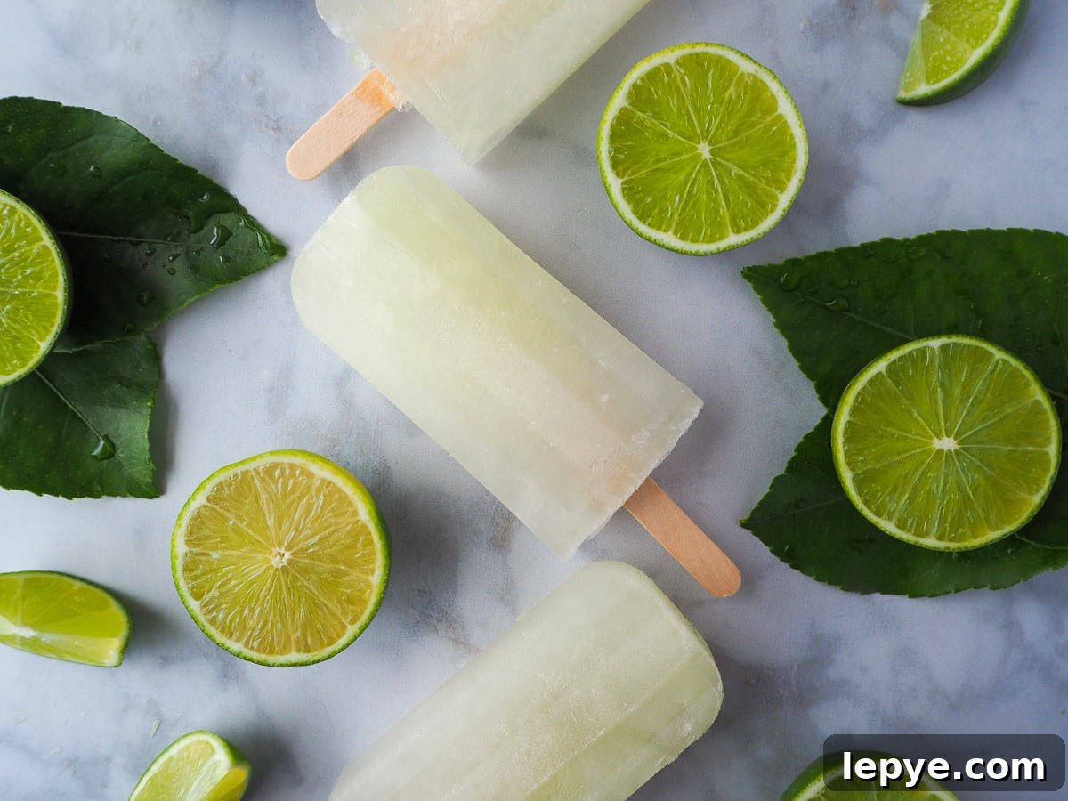 Refreshing Lime Popsicle Recipe: Homemade Citrus Ice Pops 10 Lime popsicles surrounded by fresh cut limes on a marble background.