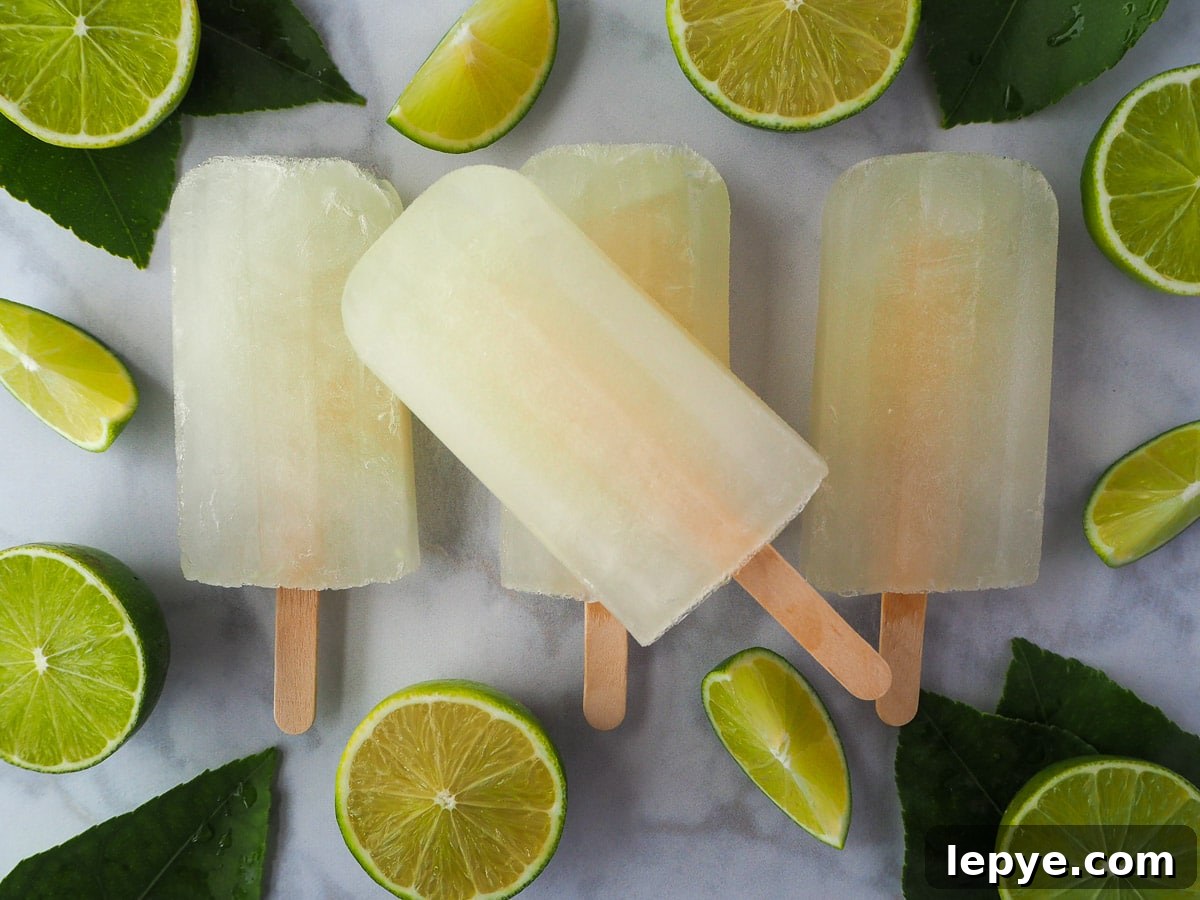 Refreshing Lime Popsicle Recipe: Homemade Citrus Ice Pops 12 Row of three lime popsicles, with a single lime popsicle on top, surrounded by fresh cut limes and leaves.