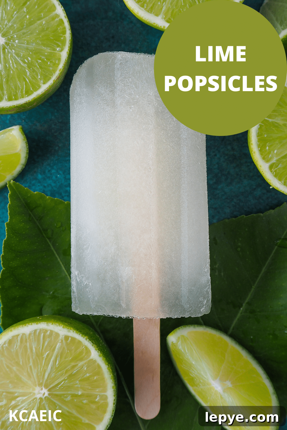 Refreshing Lime Popsicle Recipe: Homemade Citrus Ice Pops 13 Single lime popsicle on leaves, surrounded by fresh cut up limes, with text overlay, lime popsicles, KCAEIC.
