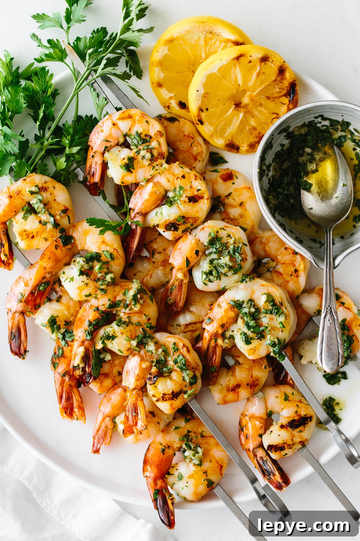 Top Memorial Day Recipes: 25+ Crowd-Pleasing Ideas 2 Grilled shrimp skewers on a plate with lemon slices, parsley and the marinade.