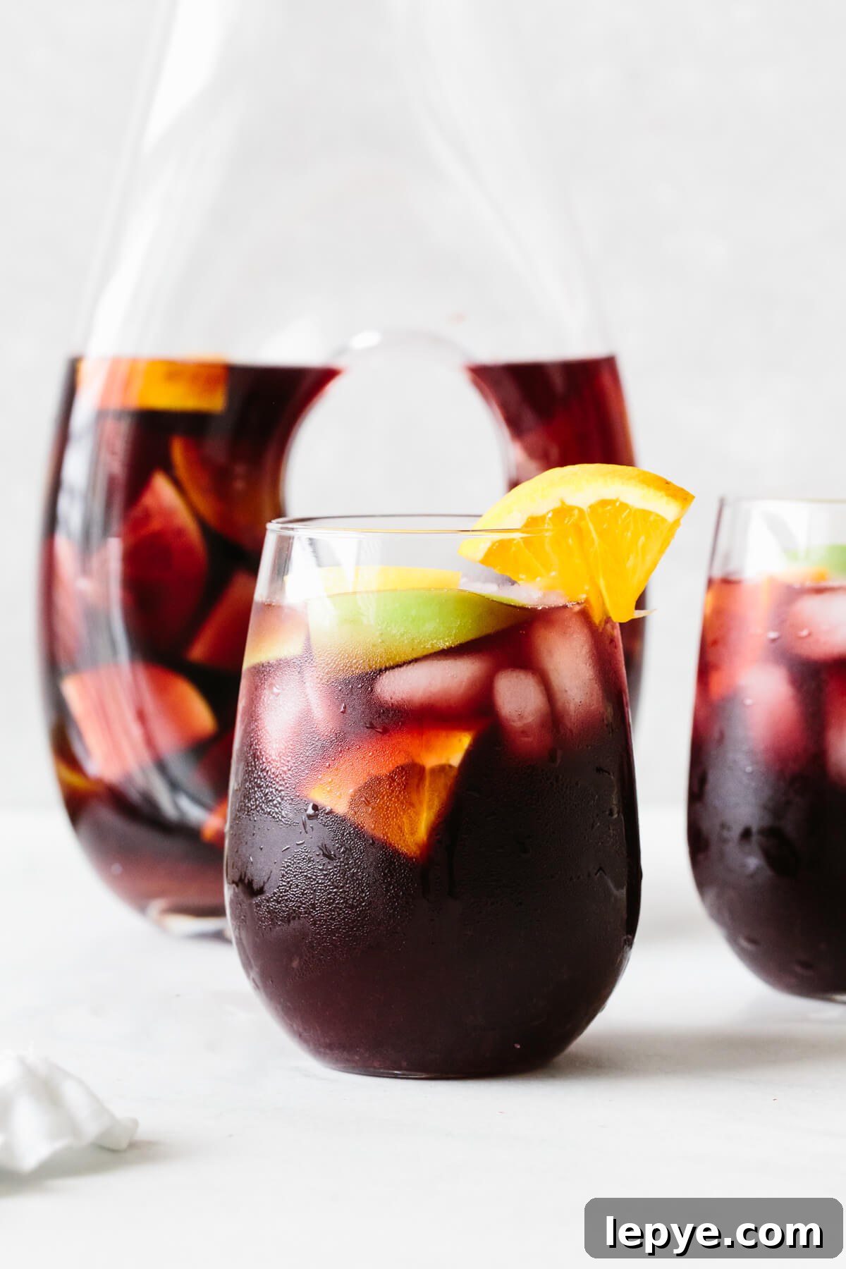 Top Memorial Day Recipes: 25+ Crowd-Pleasing Ideas 4 Red sangria in a glass with orange slice garnish and pitcher in the background.