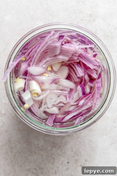 Thinly sliced onions in water in a glass jar.