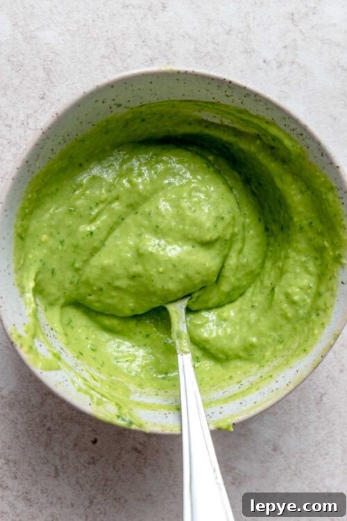 Creamy avocado cilantro lime sauce in a bowl with a spoon.