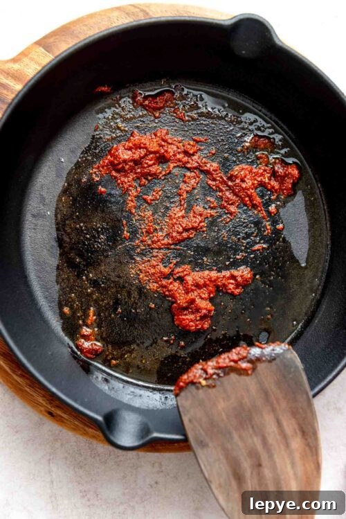 Taco seasoning and tomato paste cooking in a cast iron skillet.