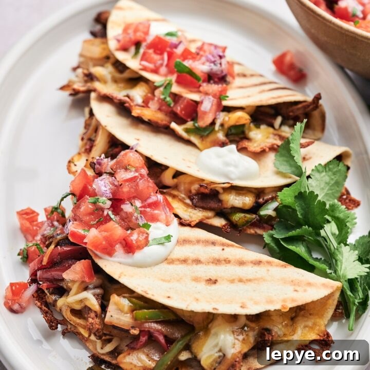 Three steak quesadillas are on a white platter. The quesadillas are topped with pico de gallo, sour cream, and fresh cilantro.