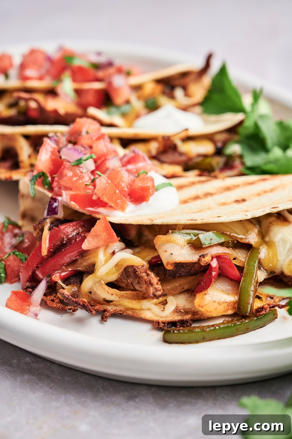 Three steak quesadillas are on a platter. The quesadillas are topped with cilantro, pico de gallo, and sour cream.