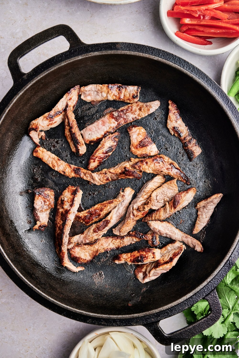 Steak strips are cooking in a large cast iron dutch oven. The steak is beginning to brown.