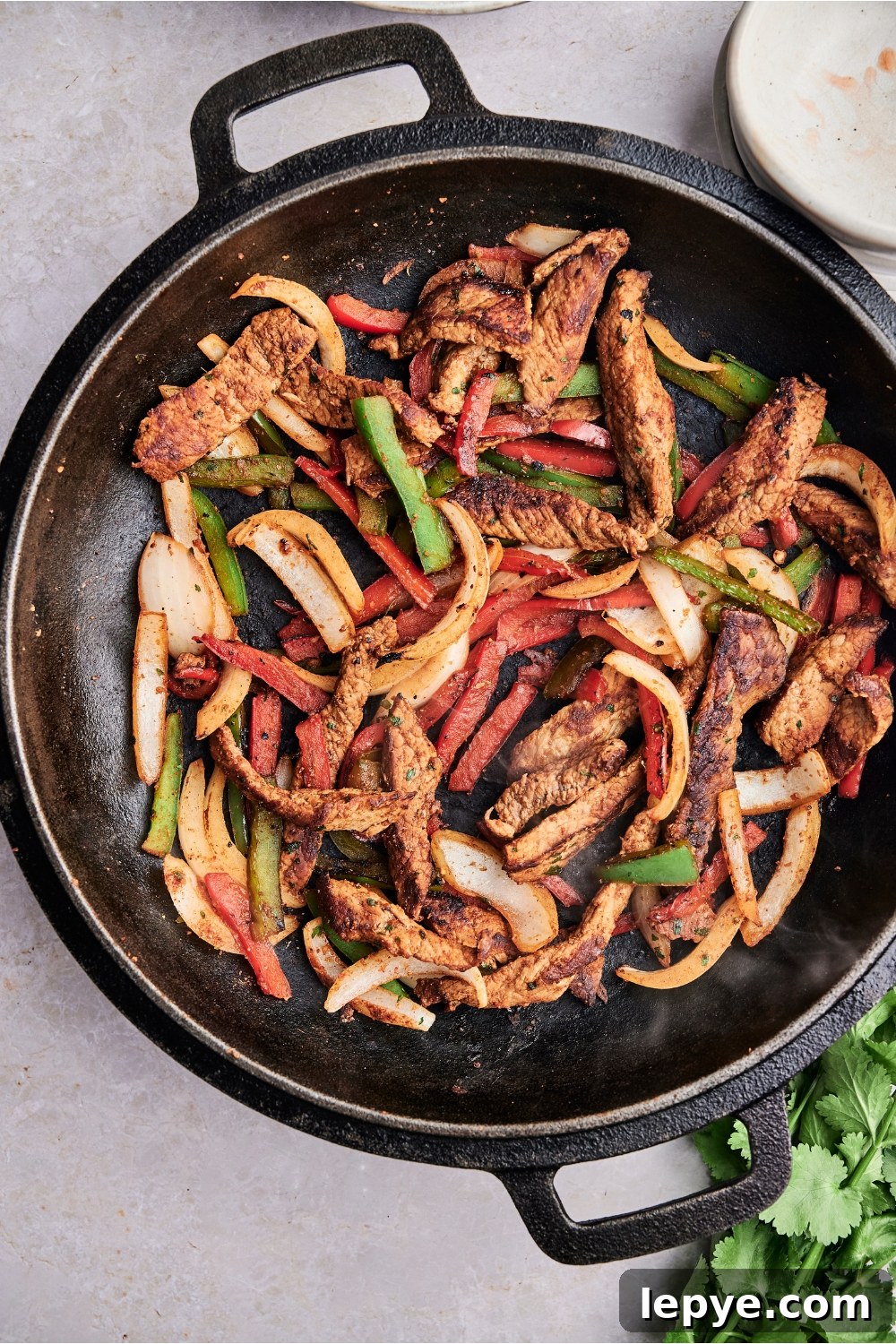 A black cast iron dutch oven holds browned steak and vegetables.