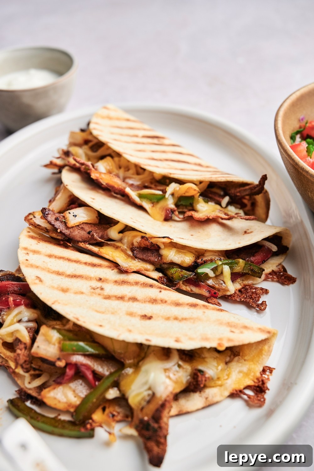 Three steak quesadillas are on a white serving platter. The quesadillas are stuffed full with steak and vegetables.