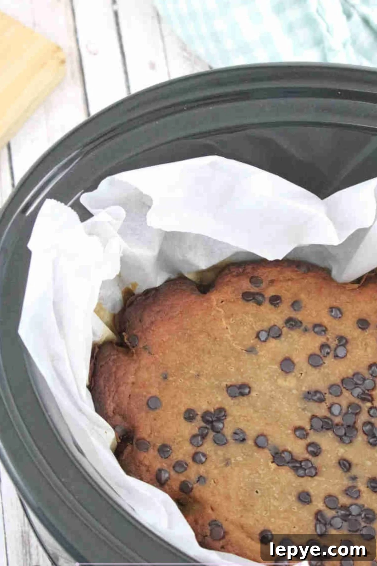 High-Protein Slow Cooker Banana Bread Recipe 2 Black slow cooker lined with parchment paper and high protein banana bread with chocolate chips in it.