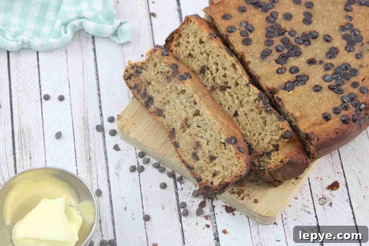 High-Protein Slow Cooker Banana Bread Recipe 14 Sliced high protein banana bread with chocolate chips on a wooden cutting board with a blue linen beside it.