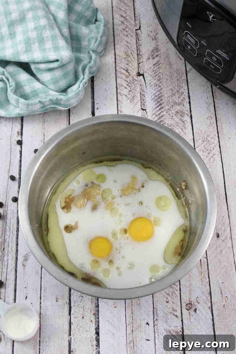 High-Protein Slow Cooker Banana Bread Recipe 4 Eggs, milk, and mashed bananas in a steel bowl with a blue linen behind it.