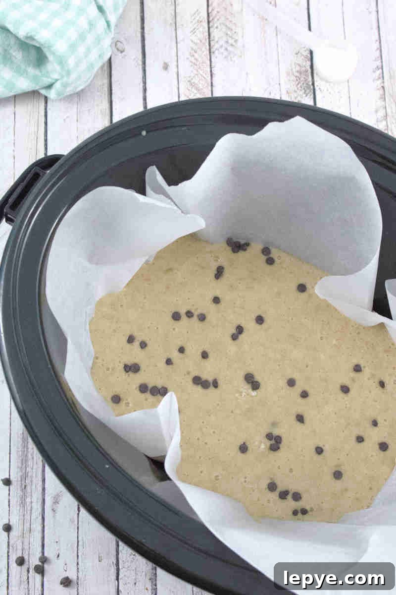 High-Protein Slow Cooker Banana Bread Recipe 7 Black slow cooker lined with parchment paper and raw high protein banana bread with chocolate chips in it.