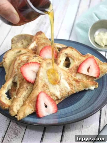 A blue plate with protein french toast in triangle slices with strawberries on it and maple syrup being poured on top.