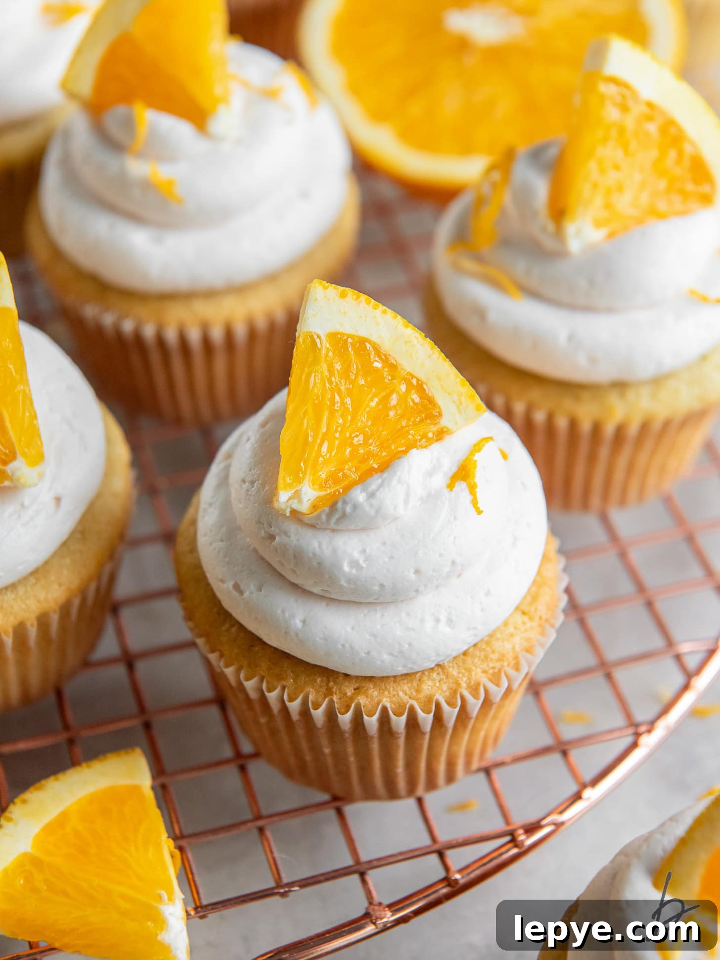 mimosa cupcake with an orange slice as garnish on wire cooling rack.