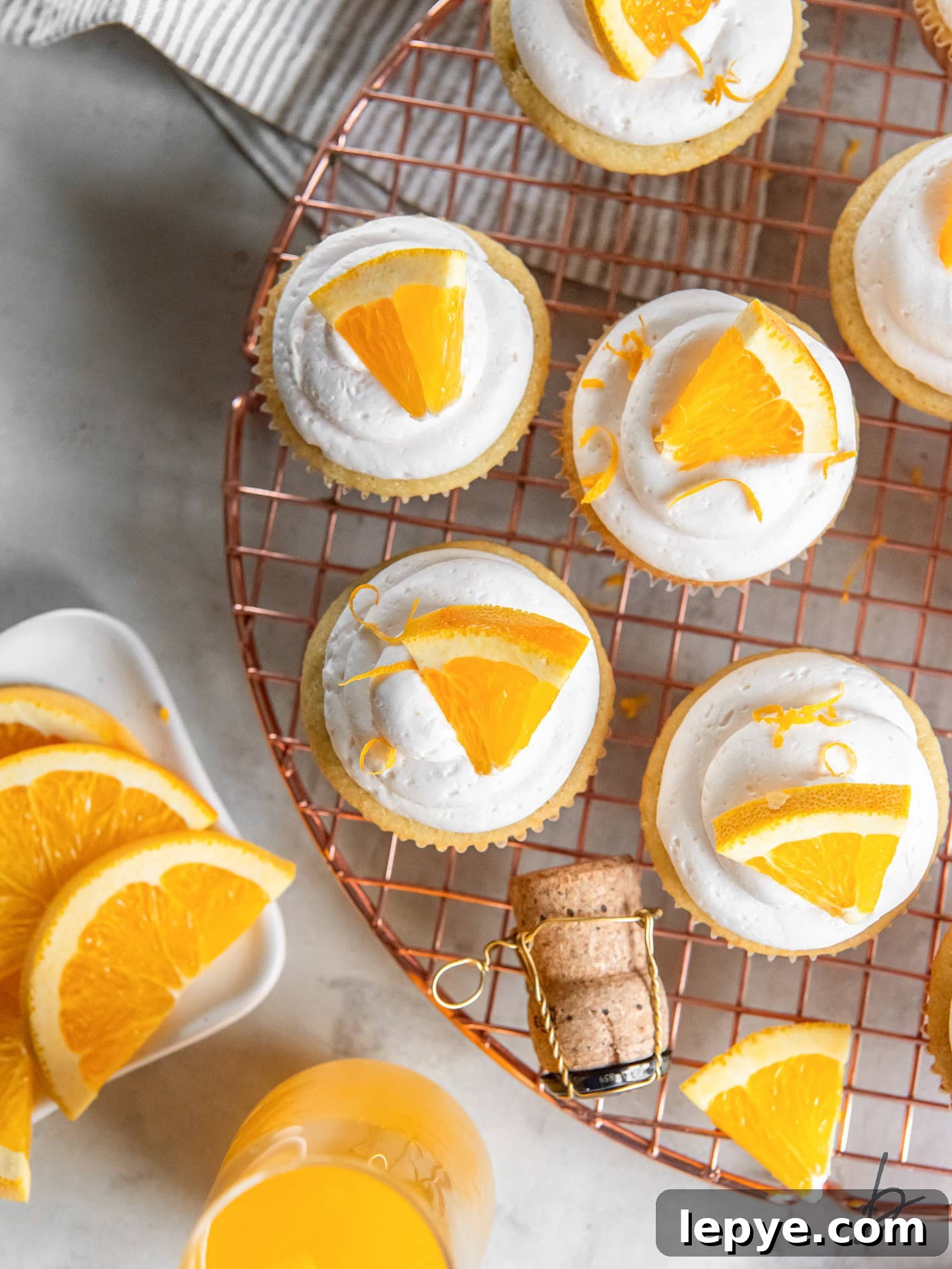 wire rack with mimosa cupcakes with champagne frosting and orange slice garnish.