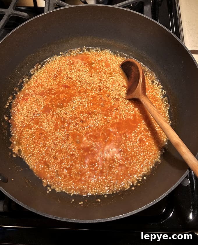Quinoa cooked with salsa in skillet with wooden spoon.
