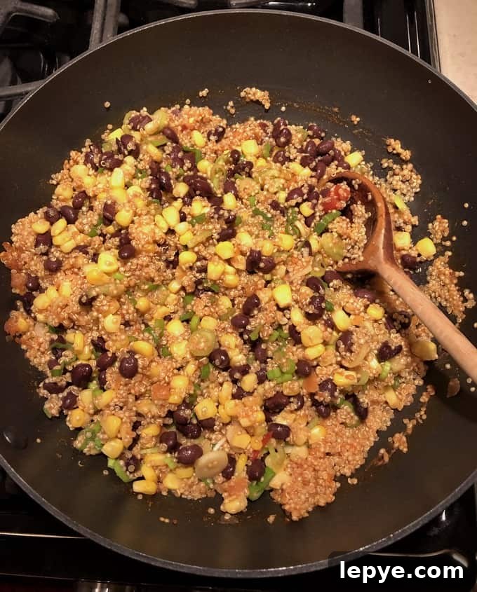 Cooking quinoa, black beans, corn, green onions with salsa in skillet.