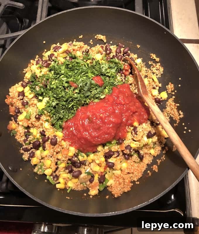 Stirring in chopped cilantro and salsa to Southwestern Quinoa Skillet with wooden spoon.