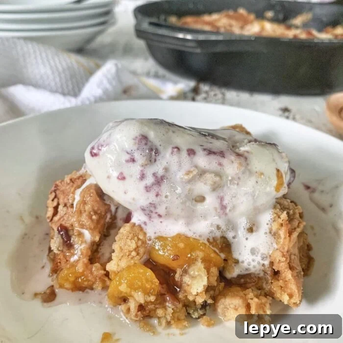 Closeup of a serving of peach dump cake with melting ice cream on top.