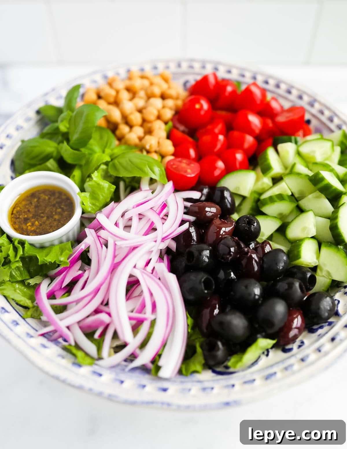 A close-up picture of a salad with onion, olives, cucumbers, tomatoes, chickpeas, basil, lettuce, and a dressing