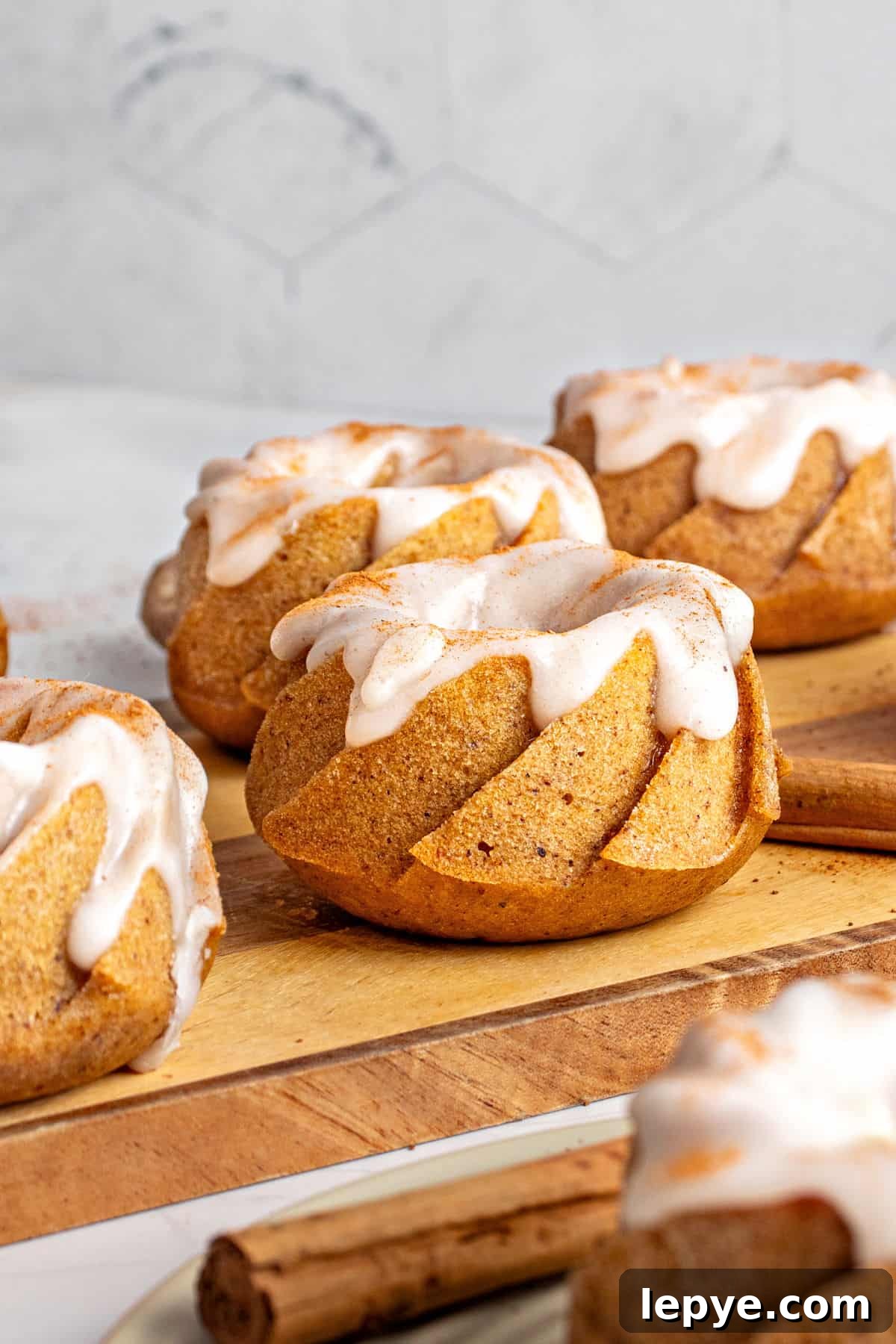 Several glazed mini pumpkin bundt cakes on a wooden board. Gray background. 