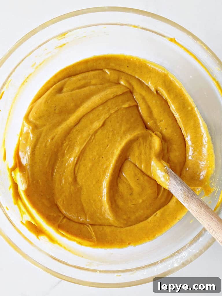 Glass bowl with pumpkin cake batter. A spatula. White surface. Top view.