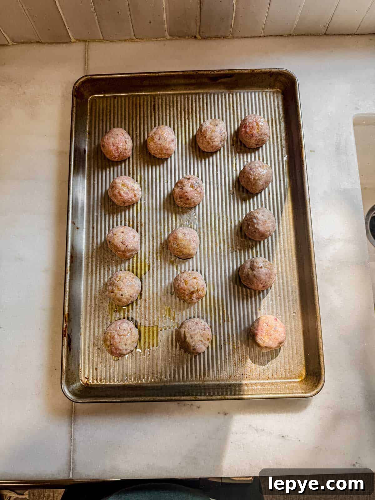 Oven-Baked Turkey Meatballs with Savory Herb Sauce 7 raw turkey meatballs arranged on a baking sheet.